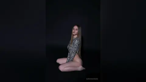 Young woman in a leopard print bodysuit posing against a dark background in a moody studio setting.
