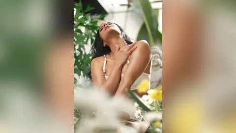 Serene woman in a white summer dress relaxing amidst lush tropical greenery and bright sunlight.