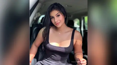 Smiling young woman in a black ribbed tank top sitting in a car on a sunny day.