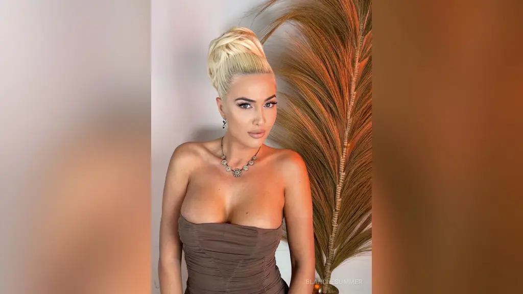 Glamorous blonde woman in a satin peach dress with wavy hair and large crystal earrings in a soft indoor setting.