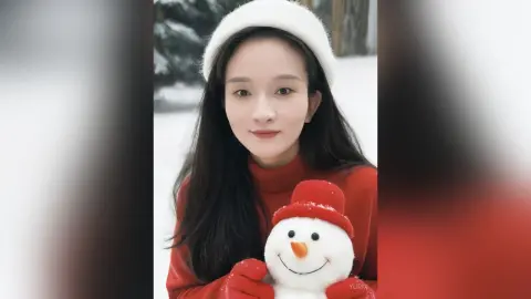 Smiling young woman in a red sweater and white beanie holding a cute snowman in a snowy winter landscape.