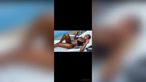 Relaxed woman in a black bikini lounging on a white sunbed by a bright blue swimming pool.