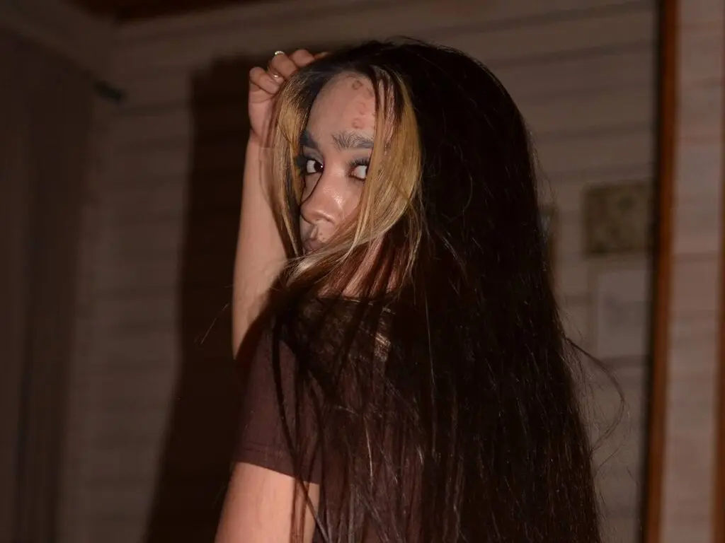 Young woman with long dark hair in a brown shirt posing in a dimly lit room with a moody atmosphere.