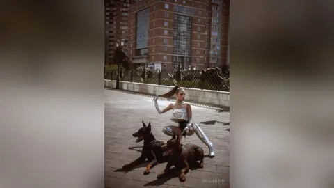 Stylish woman in a silver sequin outfit posing with a dark brown Doberman in a modern urban city setting.