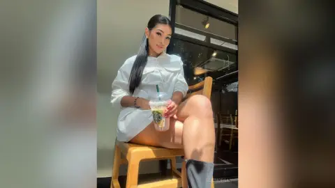 Stylish woman in a white shirt sitting at a cafe with an iced drink on a sunny day.