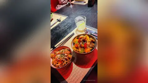 Delicious Asian stir-fry dishes served in red bowls on a dark restaurant table with chopsticks.