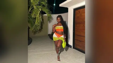 ZoeySpark poses outdoors at night wearing a bright orange and lime green two-piece outfit with strappy white sandals.
