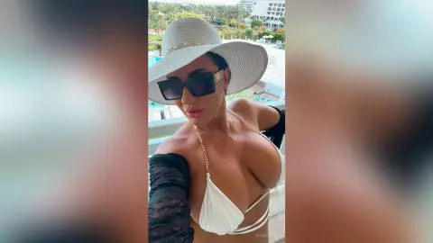 MissyJolie wears a white bikini top and a large sun hat while posing outdoors near a swimming pool.
