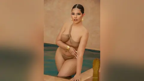 Glamorous woman in a nude bikini and gold jewelry posing by a luxury pool in a warm, sun-drenched setting.