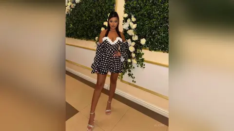 Stylish woman in a black and white polka dot off-the-shoulder mini dress posing in an elegant floral setting.
