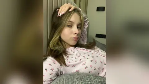 Young woman in pink floral pajama top relaxing indoors with a peaceful expression.