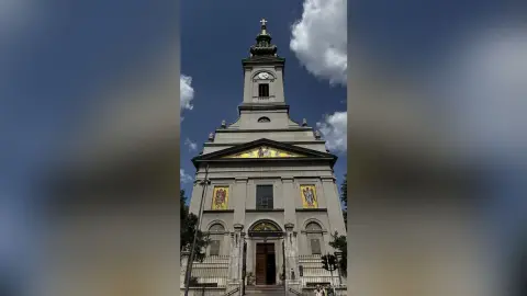 Grand neoclassical church facade with gold mosaics under a bright blue sky.