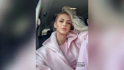 Blonde woman in a cozy pink hoodie relaxing inside a car with a serene expression.