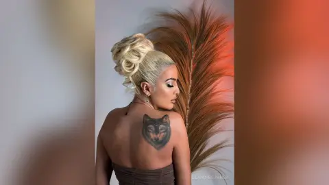 Blonde woman with a high bun and wolf back tattoo posing in a studio with warm lighting and dried pampas grass.