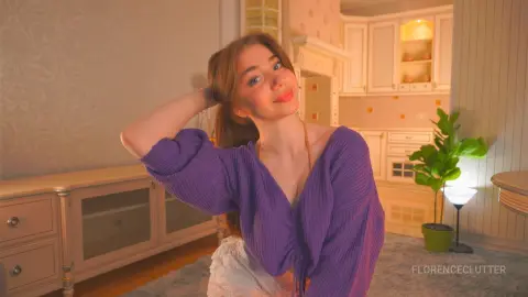 Smiling young woman in a purple knit sweater relaxing in a warm, cozy living room setting.
