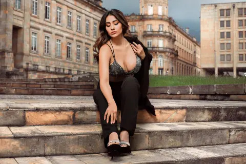 Stylish woman in a black crop top and trousers sitting on stone steps in front of historic European architecture.