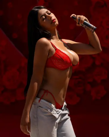 Young woman in a red lace bikini top and light denim jeans posing against a vibrant red floral background.