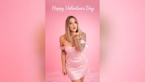 Blonde woman in a pink satin dress blowing a kiss against a pink background for Valentine's Day.