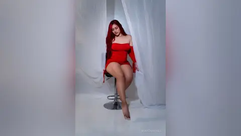 Elegant woman in a red cocktail dress posing against white curtains in a bright, minimalist studio setting.