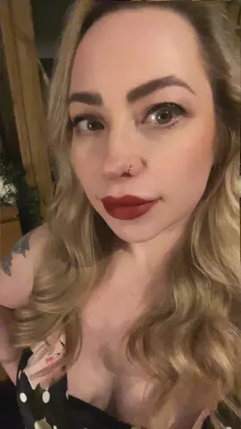 FrankiiRayeXXXX looks into the camera with red lipstick and blonde hair, wearing a black polka-dot top.