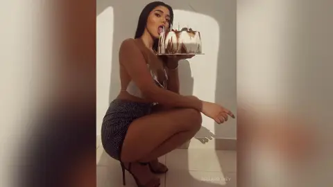 Young woman in a sparkly silver outfit eating cake in a minimalist indoor setting with soft lighting.