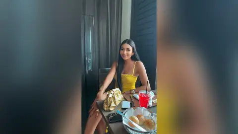 Smiling woman in a yellow summer dress sitting at a restaurant table with a red drink and snacks.