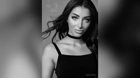 Elegant woman with long wavy hair wearing a black choker and tank top in a moody black and white portrait.