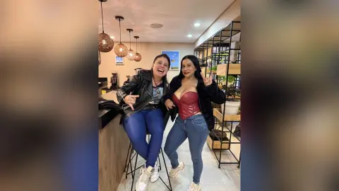Two happy women in leather jackets and jeans laughing together in a modern cafe setting.
