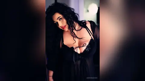 AdiraMaeven poses in a black sheer babydoll, showing off her cleavage and long, dark wavy hair.