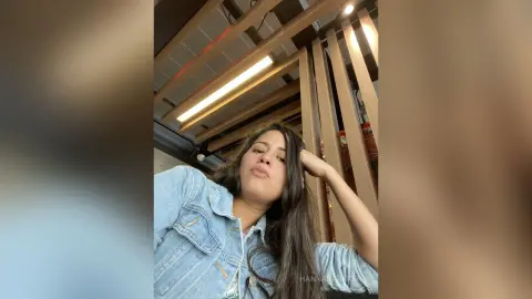 Young woman in a light denim jacket relaxing in a modern room with warm ambient lighting.