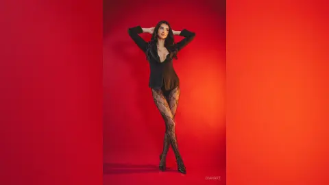 Elegant woman in a black blazer and patterned tights posing confidently against a vibrant red studio background.