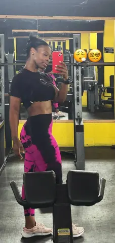Fit woman in black crop top and pink patterned leggings posing in a gym mirror for fitness motivation.