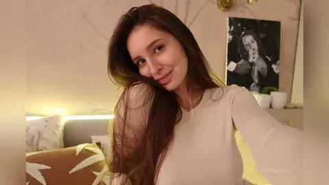 OliviaHardies smiles at the camera while leaning back in her bed with her long brown hair flowing over her shoulders.