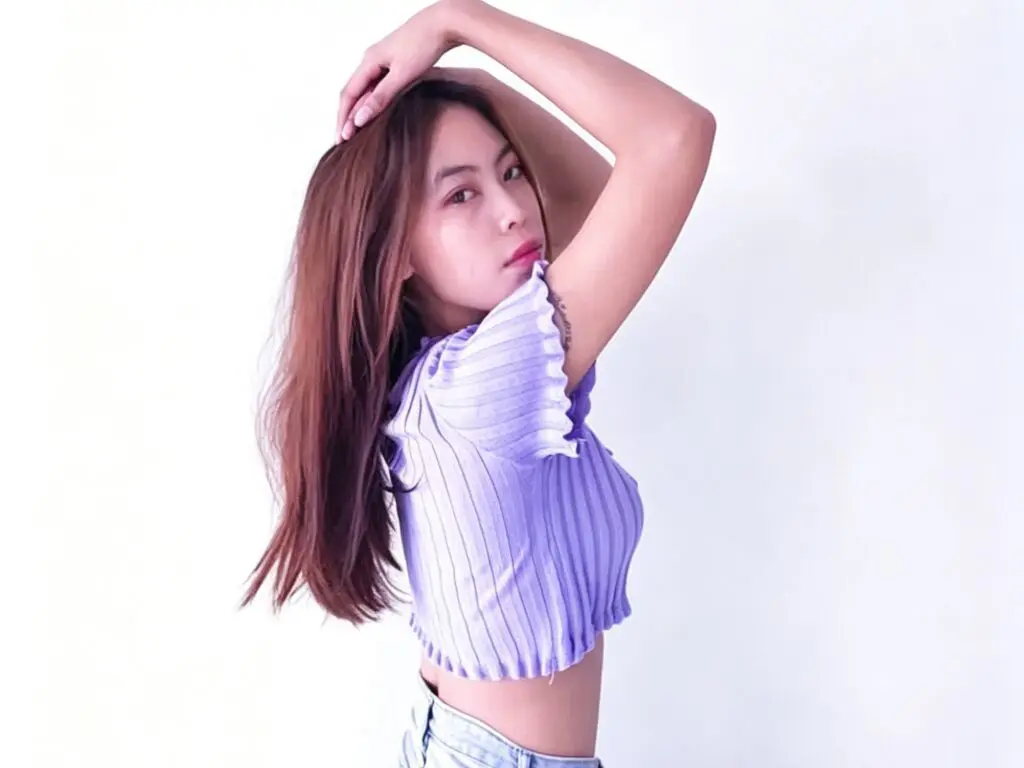 Young woman in a purple ribbed crop top posing against a white background with a relaxed, stylish mood.