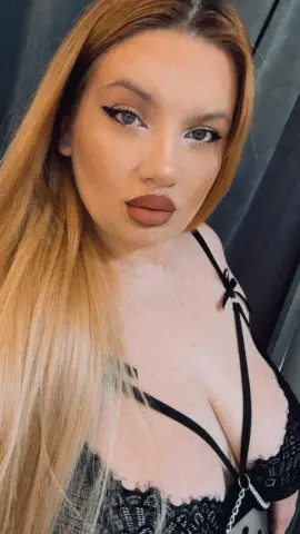 Blonde woman in black lace lingerie posing with winged eyeliner for a glamorous close-up portrait.