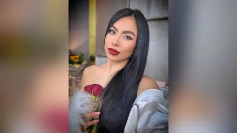 Glamorous woman with long dark hair and bold red lipstick holding red roses in a soft, elegant setting.