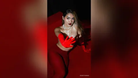 RosieThomas — Glamorous woman in red outfit and pearl necklace posing under moody red studio lighting.