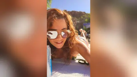 Smiling woman in sunglasses relaxing on a sunny beach under bright sunlight.