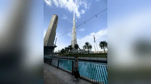 Stylish woman in a patterned dress standing by a blue pool with the Burj Khalifa skyscraper in Dubai.