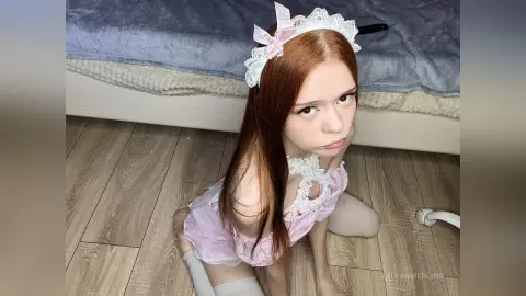 Young woman in a pink lace frilled outfit sitting on a floor in a cozy indoor setting.