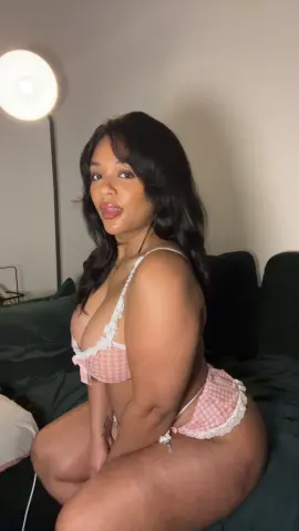 Hazelvalentine poses in a pink checkered lace bra and matching panties, showing off her curves while sitting on a dark bed.