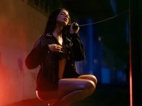 Moody portrait of a woman in a black studded jacket posing outdoors at night under red and blue lighting.