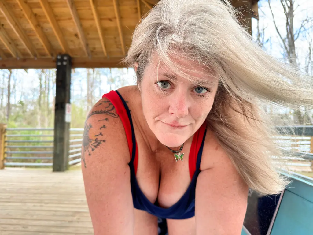Blonde woman in a blue tank top relaxing on a turquoise wooden bench outdoors on a sunny day.