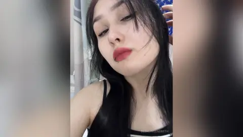 Young woman with long dark hair and red lipstick posing in a casual indoor setting.