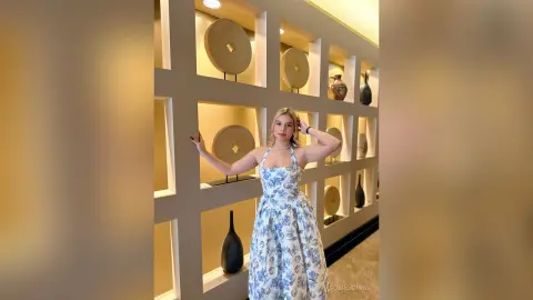 Elegant woman in a blue floral halter dress posing in a luxury interior with modern decor.