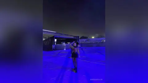 Stylish woman in a black outfit posing under blue neon lights at a night rooftop party.