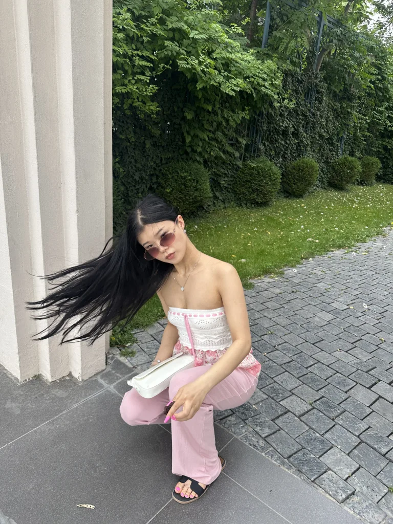 TinaxKim smiles at the camera with long black hair and a silver necklace against a patterned wall.