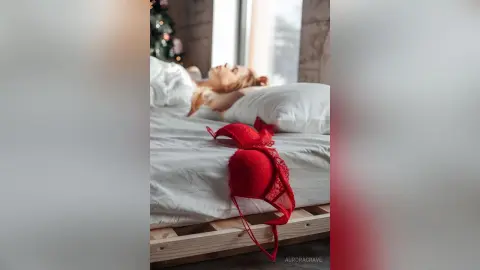 Blonde woman relaxing in bed with red lace lingerie in a bright, cozy bedroom setting.