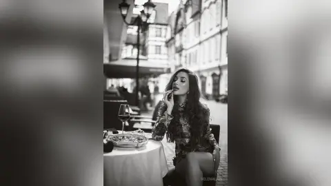 Elegant woman in a patterned dress dining at an outdoor cafe in a vintage European street setting.
