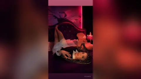 Woman with long braids relaxing in a dark bedroom with moody red lighting.